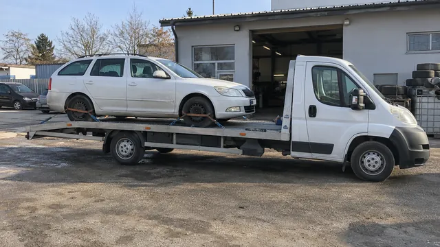 Bílý odtahový vůz s upevněným vozidlem Škoda na hliníkové plošině